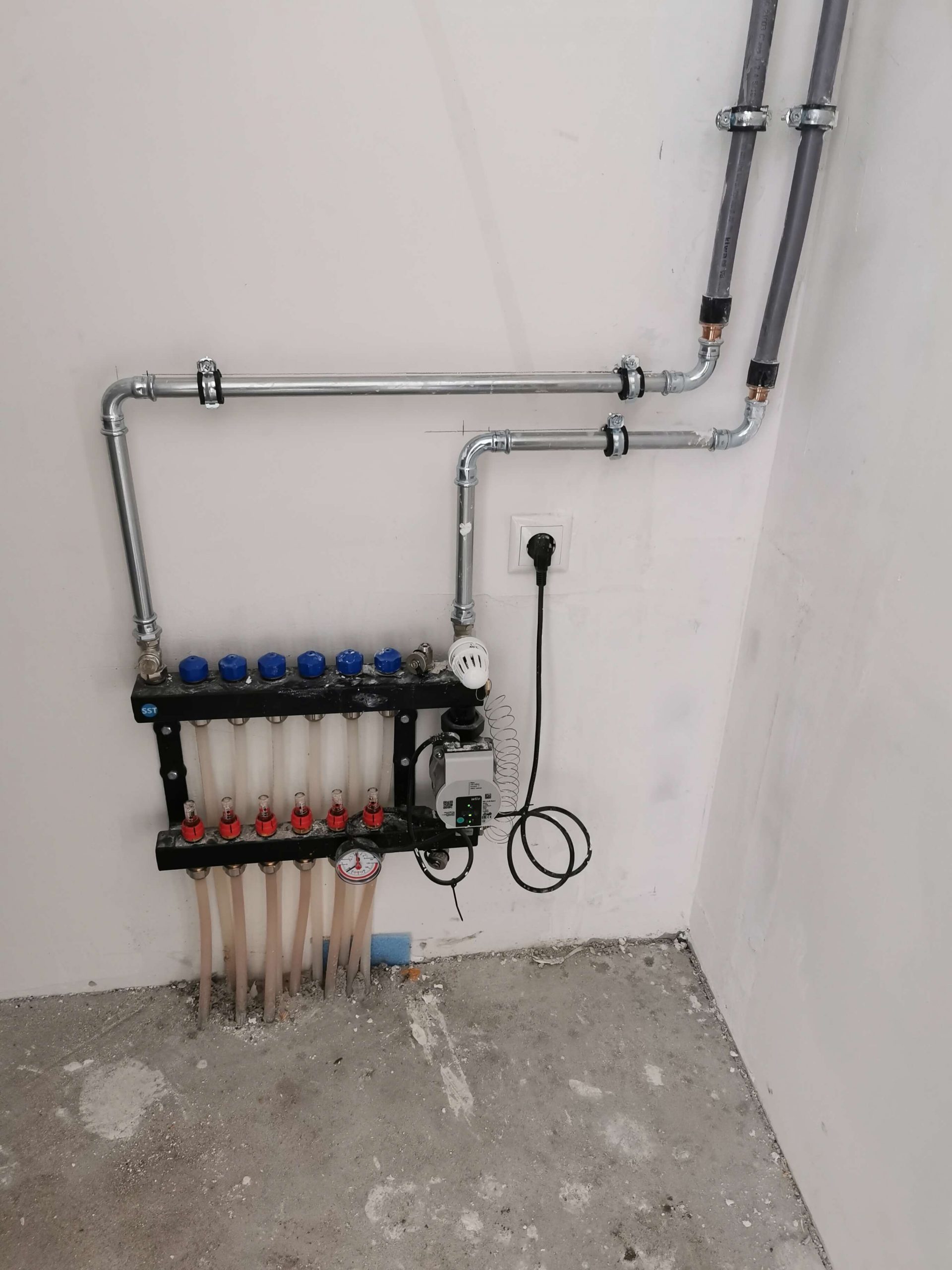 Verdeler voor vloerverwarming met circulatiepomp, aangesloten op de wand in een woning in Limburg